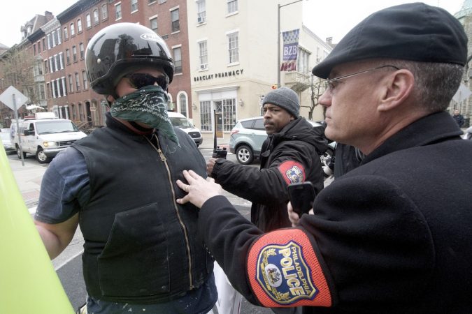 A member of the Philadelphia Police Department's civil affairs unit requests an unidentified and masked person, not related to the gathering, to keep a distance as a group of people protest outside a Starbucks on 18th and Spruce streets in Philadelphia over Thursday's controversial arrests of two black men there. (Bastiaan Slabbers/for WHYY)