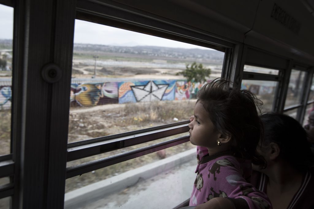 Mexico Migrants Caravan A Central American child who is traveling with a caravan of migrants, peers at the border wall from a bus carrying the group to a gathering of migrants living on both sides of the border, in Tijuana, Mexico, on April 29. (AP Photo/Hans-Maximo Musielik)
