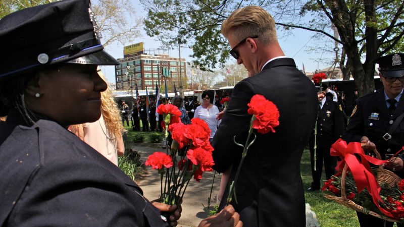 Police officers and firefighters hand out red carnations to participants in the Living Flame Memorial Service. (Emma Lee/WHYY)