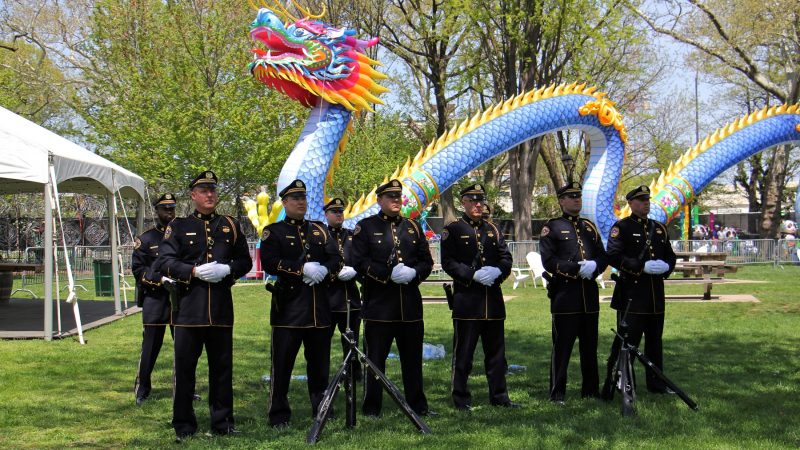The Philadelphia Police and Fire Honor Guard stand at ease during the memorial ceremony, set against the backdrop of the Chinese Lantern Festival in Franklin Square. (Emma Lee/WHYY)