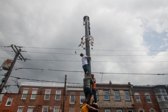 Nick Cordisio climbs on to his teammates shoulders and tosses a piece of cured meat that hung from the top of the grease pole. (Brad Larrison for WHYY)