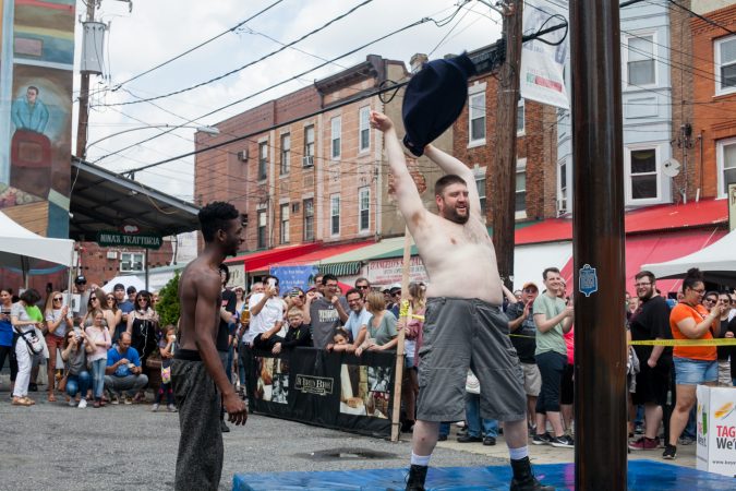 Tyler Dallas, left, and Mike Sirera were the first two volunteers to attempt the grease pole contest at the Italian Market Festival Saturday. (Brad Larrison for WHYY)