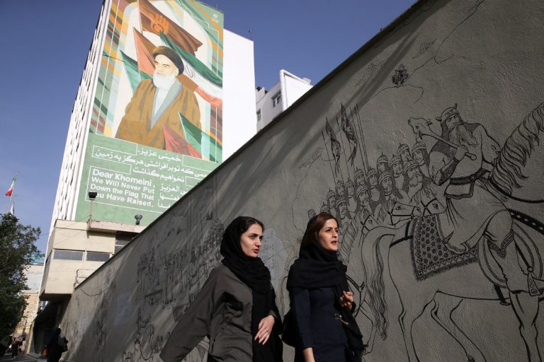 Iranian women walk past a portrait of the late revolutionary founder Ayatollah Khomeini and paintings of Persian poetry in Tehran, Iran, Monday, May 7, 2018. (Vahid Salemi/AP Photo)