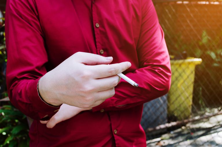 A man in a red shirt holds a lit cigarette in his right hand