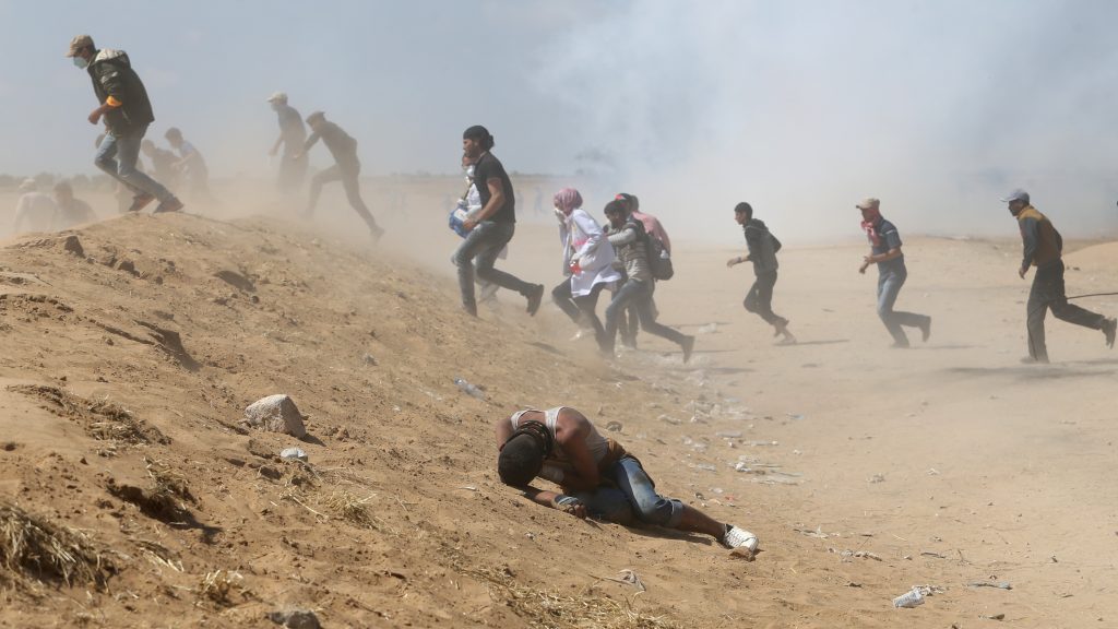 Palestinian demonstrators run or take cover from tear gas fired by Israeli forces at the Israel-Gaza border. (Ibraheem Abu Mustafa/Reuters)