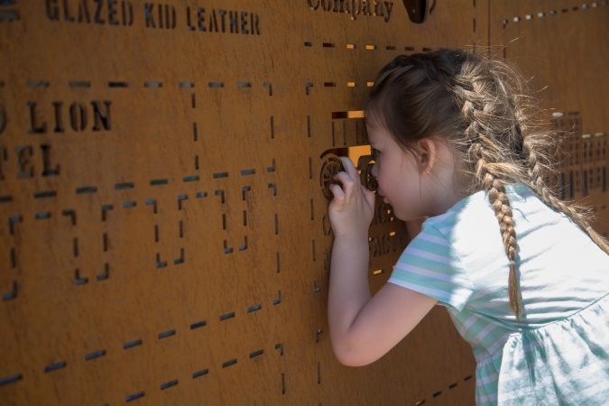 Cecilia Norris, 3, takes a peek through the cutouts in the iron picture map of the city of Philadelphia that greets visitors as they enter the first phase of the Philadelphia Rail Park June 14th 2018. (Emily Cohen for WHYY)