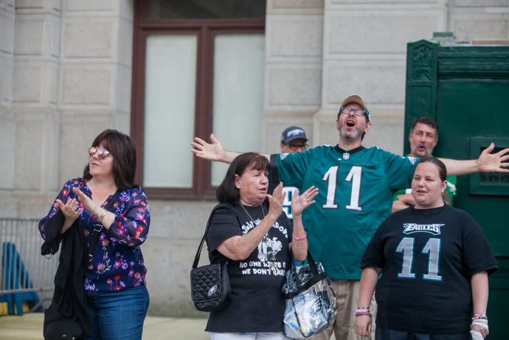 2018 06 05-b larrison city hall philadelphia- eagles fans rally at city hall after president trump cancels event at white house-4 Mary Velez, center, her daughter Elen, right, and other Eagles fans sing the team's fight song at a rally for the team at City Hall Tuesday evening a day after President Trump canceled an event at the White House to honor the Super Bowl Champions. (Brad Larrison for WHYY)