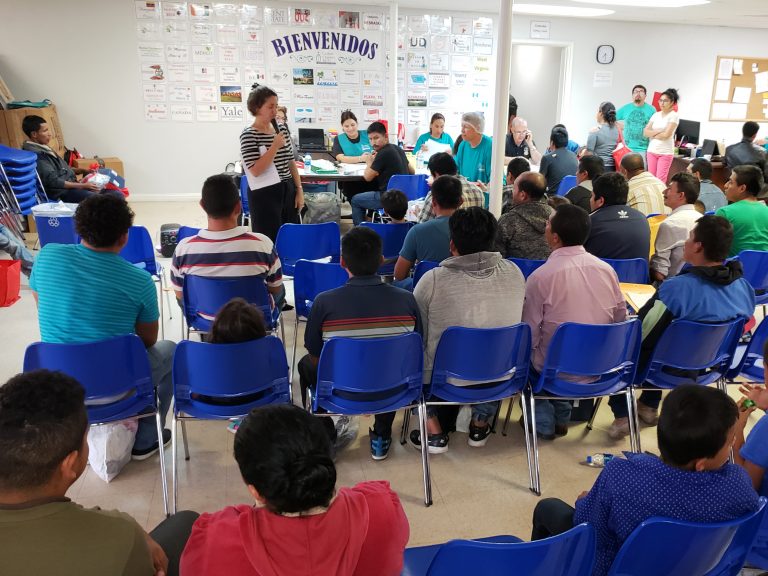 About 100 newly arrived immigrants listen to a volunteer walk them through the process to seek asylum at a Catholic Charities respite center in McAllen, Texas. (Mose Buchele/KUT)
