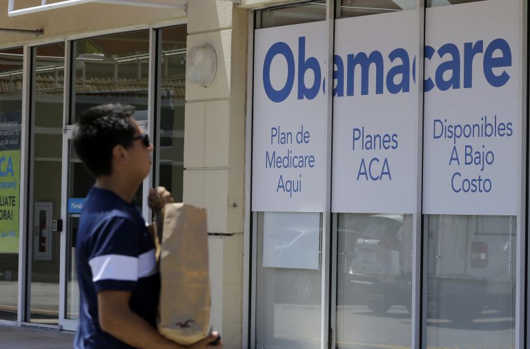 This photo taken Thursday, July 27, 2017, shows a man walks by an healthcare insurance office in Hialeah, Fla.