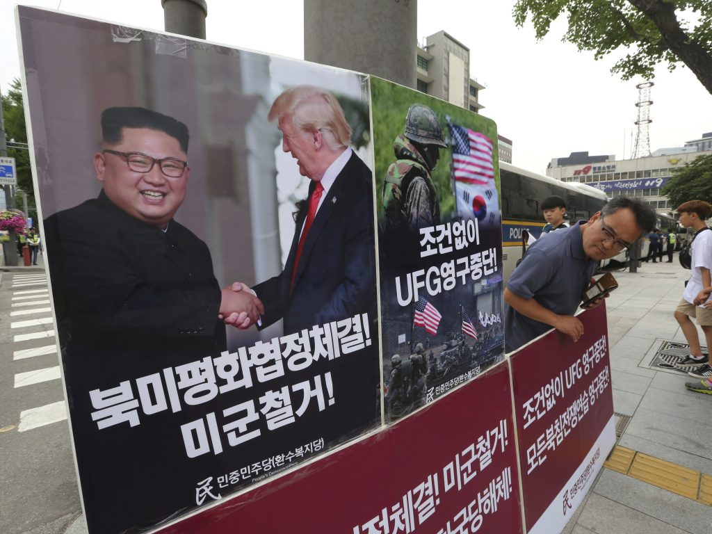 A photo of President Trump and North Korean leader Kim Jong Un is on display as a member of People's Democratic Party stands in opposition of military exercises between the United States and South Korea near the U.S. embassy in Seoul on Tuesday. (Ahn Young-joon/AP)