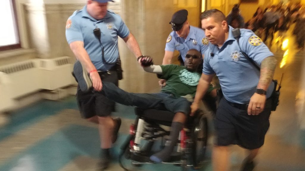 ejection Philadelphia sheriff's deputies eject a protester from City Council chambers Thursday after he and others staged a die-in to protest a lack of housing for those with disabilities. (Tom MacDonald/WHYY)