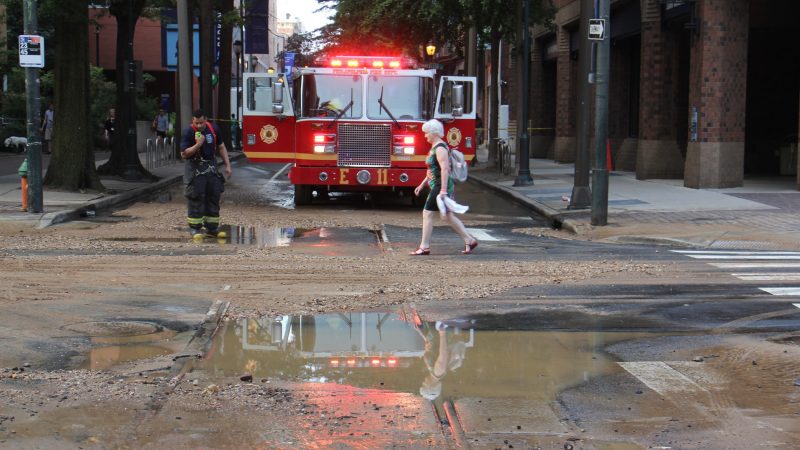 A pedestrian crosses the street at 11th and Walnut streets after a water main break left Center City streets covered with water and debris. (Emma Lee/WHYY)