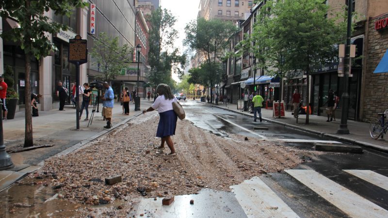 A pedestrian at Walnut and Juniper streets steps over a pile of debris left behind by a massive water main break in Center City. (Emma Lee/WHYY)