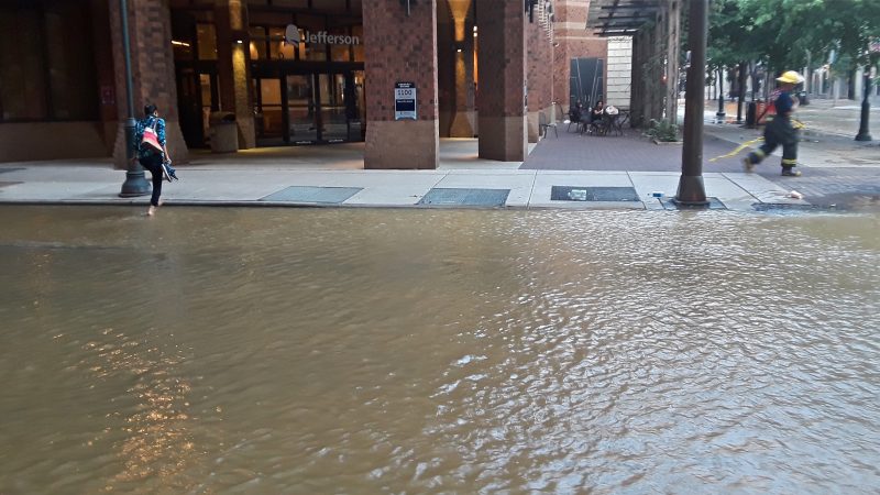 A woman took off her shoes and rolled up her pants to cross 11th street after a water main break flooded several Center City streets. (Trenae NUri/WHYY)