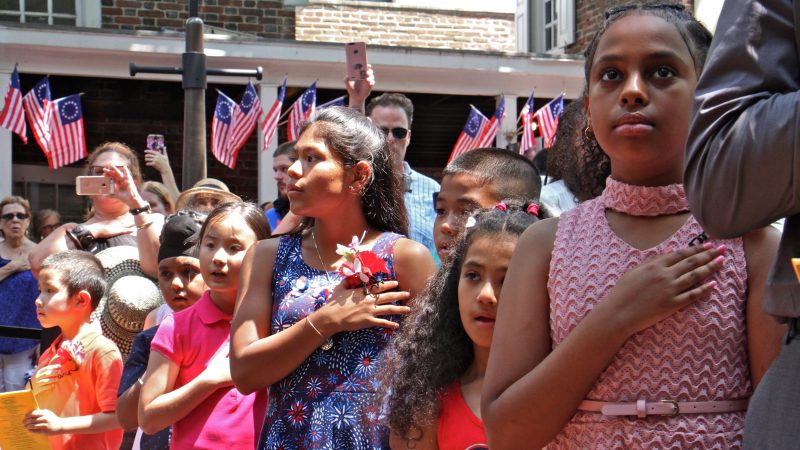 Angelica Wendel (center) of Malvern, originally from Guatemala, says the Pledge of Allegiance for the first time as a U.S. citizen. She was one of 13 children who became a U.S. citizen during a ceremony at the Betsy Ross House. (Emma Lee/WHYY)