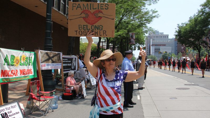 Marlena Santoyo and other protesters from the Brandywine Peace Community wave signs and banners on Market Street during the Independence Day parade. (Emma Lee/WHYY)
