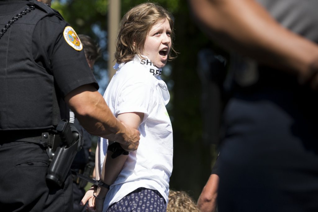2018 07 15 – r wisniewski – protestors police – leesport berks detention – vigil arrest 3 A demonstrator is arrested at the Vigil to Shut Down Berks on the afternoon of July 15. Seventeen arrests were made after group blocked a road outside the detention facility in Leesport, Pa., which is used to house immigrant families who are fighting deportation.