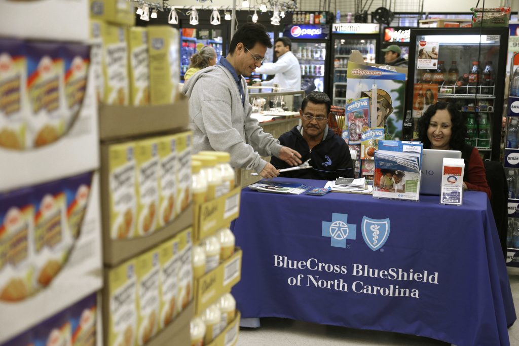 AP Poll Hispanic Health Care In this file photo taken Nov. 22, 2014, Blue Bridge Benefits LLC agent Patricia Sarabia, right, and Adolfo Briceno, left, with Spanish Speaking LLC, help a potential customer with Blue Cross Blue Shield at a kiosk promoting Obama Care at Compare Foods in Winston-Salem, N.C. A new poll finds that more than half of Hispanic adults have encountered a communication barrier in the health care system. (AP Photo/Gerry Broome, file)