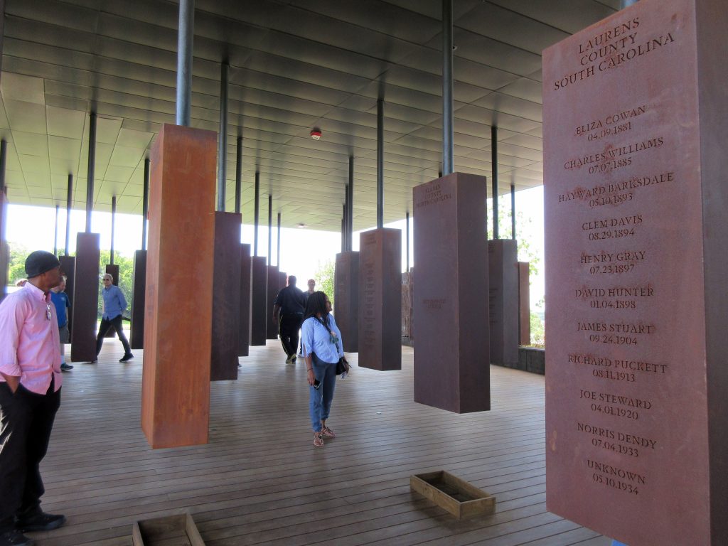 Travel Montgomery This April 28, 2018 photo shows visitors looking at markers bearing the names of lynching victims at the National Memorial for Peace and Justice in Montgomery, Ala. The memorial includes some 800 markers, one for each county in the U.S. where lynchings took place, documenting the killings of more than 4,400 individuals between 1877 and 1950. (AP Photo/Beth J. Harpaz)