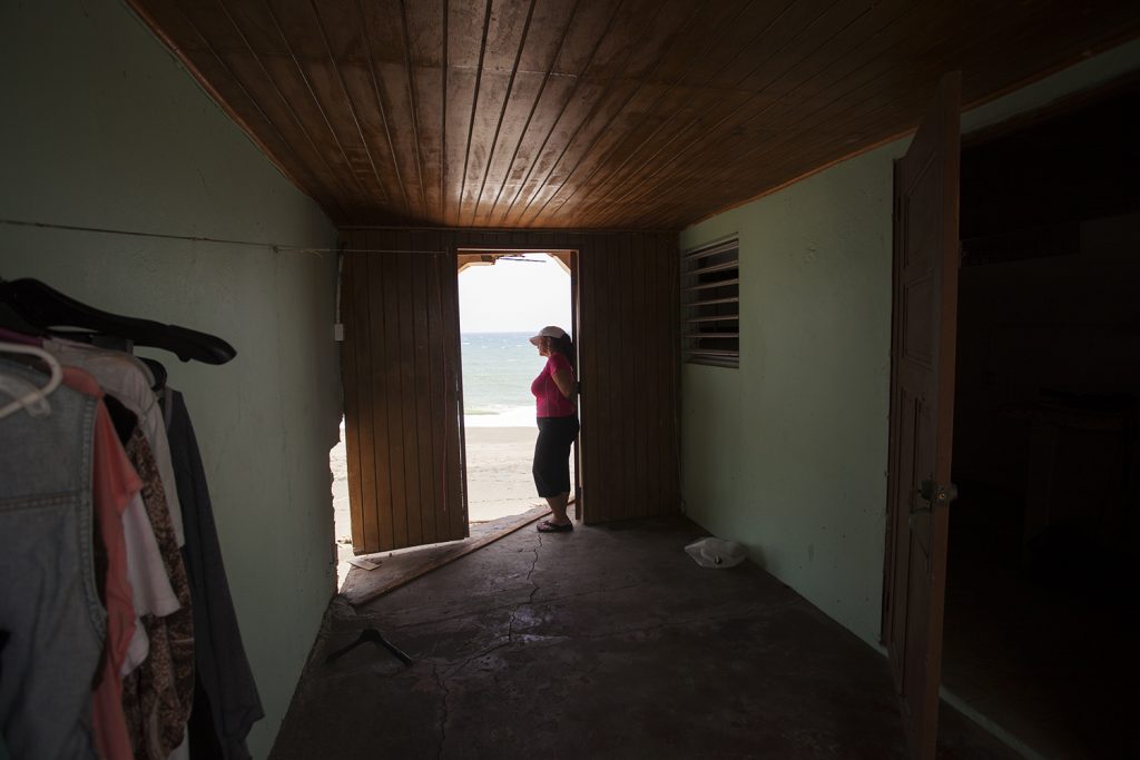 IMG_4616 Rosa Elena Mastache Dominguez looks out at the beach through a door that once led to the back of her family home. Hurricane Maria shrunk the beach behind her home, then another storm brought waves that destroyed the structure. (Irina Zhorov/WHYY)