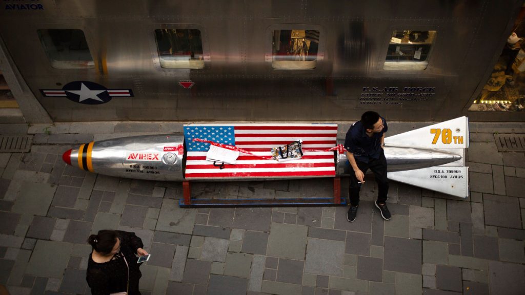 trade16x9 A man sits on a promotional gimmick in the form of a bomb and the U.S. flag outside a U.S. apparel shop at a shopping mall in Beijing. China says it’s girded for a trade war with the U.S. and can give as good as it gets, but behind the official bravado lies a deep unease over trade friction with Washington. (AP Photo/Mark Schiefelbein)