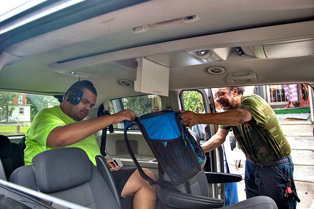 09 07 2018-e cohen taxi school transport-7 Linwood Bellamy (right) hands his son, Kareem Bellamy, 20, his lunch bag as he loads into the taxi that will take him to school. An increasing number of Philadelphia students are relying on cabs to transport them to and from school. (Emily Cohen for WHYY)