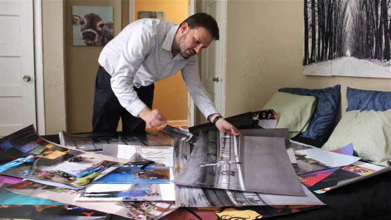 Steve Garguilo lays out photographs taken by Tunisian photographer Sophia Baraket, who died unexpectedly while the exhibit was being planned. (Emma Lee/WHYY)