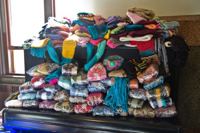 Donated scarves and hats are stacked on top of a piano at the annual Knit In at Philadelphia City Hall. (Kimberly Paynter/WHYY)