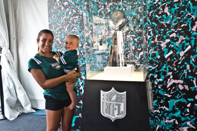 Francesca Tiedeken and her son Matthew Jr., 10 months-old, take a photo with the Lombardi Trophy at a Penn’s Landing celebration of the opening of football season. (Kimberly Paynter/WHYY)