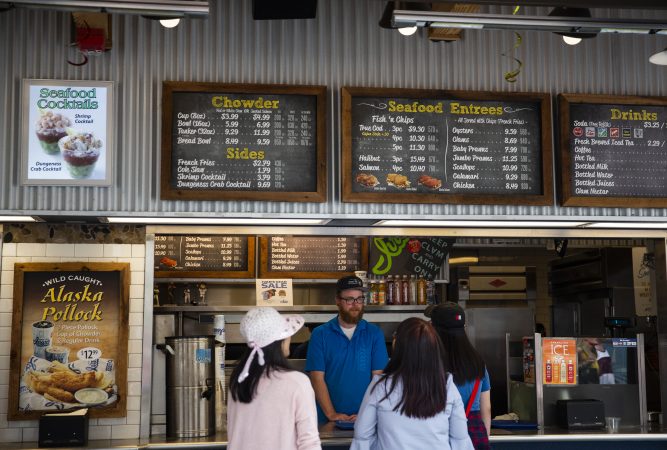 Tyler Bell, (center), who has worked at Ivar's Fish Bar on the waterfront for two years, takes an order from customers on Wednesday, August 15, 2018 in Seattle, Washington.  (Lindsey Wasson for the Inquirer)