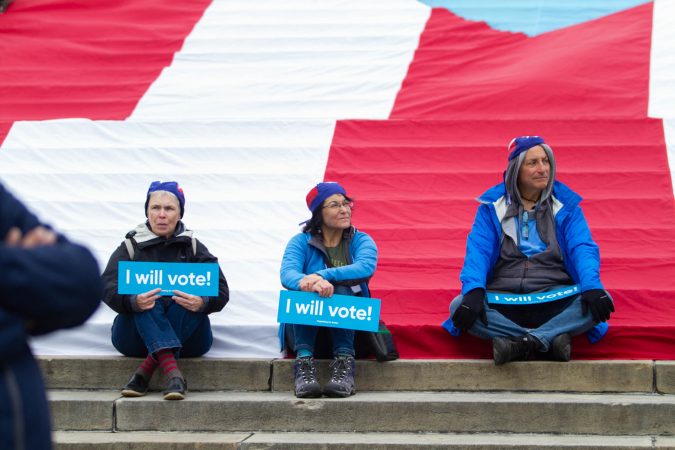 Protesters hold down a large Puerto Rican flag that was laid it at the steps of the Philadelphia Museum of Art to commemorate the people who died in Hurricane Maria in Puerto Rico. (Miguel Martinez for WHYY)