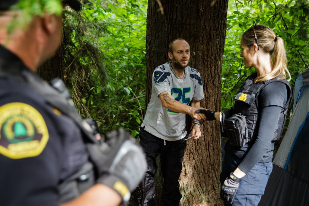 Social worker, Lauren Rainbow (right), along with Police Officer Mike Buell (left) meet a man illegally camped in the woods in Snohomish County. They are part of a new program in the county that helps people with addiction, instead of arresting them. Social worker, Lauren Rainbow (right), along with Police Officer Mike Buell (left) meet a man illegally camped in the woods in Snohomish County. They are part of a new program in the county that helps people with addiction, instead of arresting them. (Leah Nash for Finding Fixes Podcast)