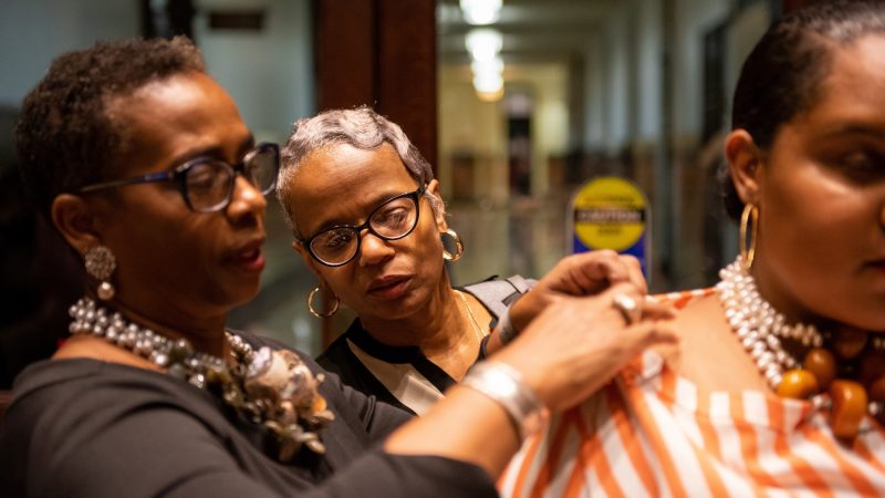 Donna Thomas looks on as her sister-in-law, designer Julia Turner Lowe of JTL Designs, makes adjustments before the Friday night runway show at Philadelphia Fashion Week, held at Dilworth Park. (Kriston Jae Bethel for WHYY)