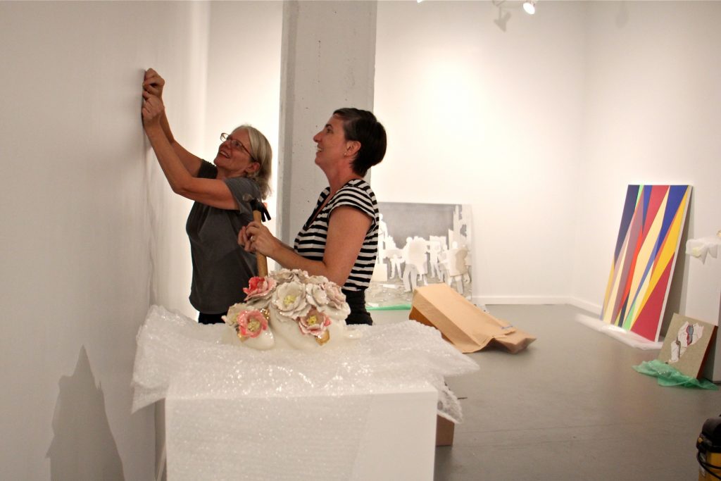 52017 08 02-e lee-jane irish mary henderson-philadelphia crane arts-artists displaced by vox building fire Jane Irish (left) and Mary Henderson of Tiger Strikes Asteroid galleries hang their first show at the Crane Arts Building. (Emma Lee/WHYY, file)