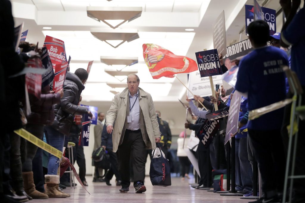 A pedestrian walks through a hallway as supporters of Democratic U.S. Senate candidate Bob Menendez, left, rallied against supporters of Republican candidate Bob Hugin outside of the NJTV Studios where the two are scheduled to engage in a debate, Wednesday, Oct. 24, 2018, in Newark, N.J. (AP Photo/Julio Cortez)