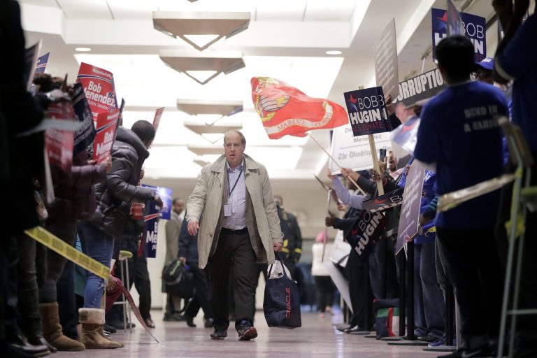 A pedestrian walks through a hallway as supporters of Democratic U.S. Senate candidate Bob Menendez, left, rallied against supporters of Republican candidate Bob Hugin outside of the NJTV Studios where the two are scheduled to engage in a debate, Wednesday, Oct. 24, 2018, in Newark, N.J. (AP Photo/Julio Cortez)