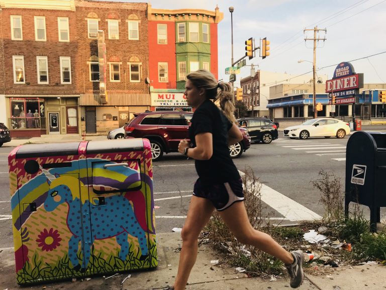 A woman runs past a pile of litter next to a Big Belly trash can on South Broad Street. (Ariella Cohen/WHYY)