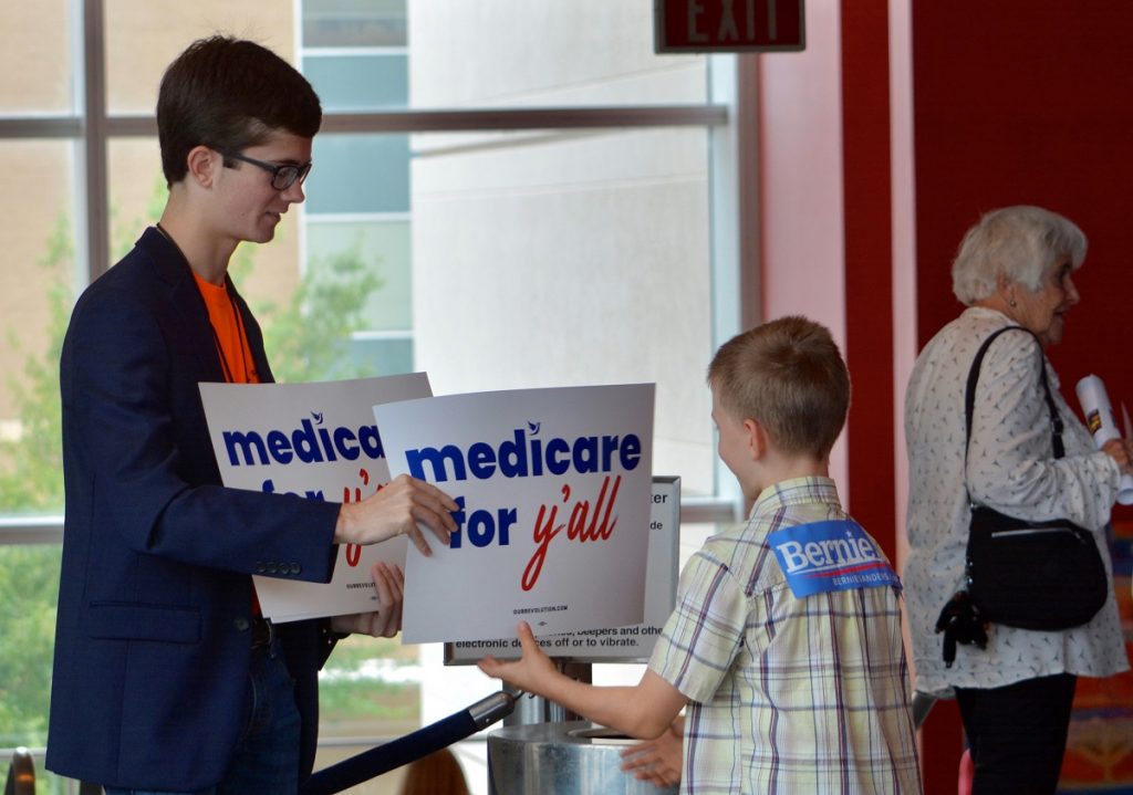 Election 2018 Bernie Sanders South Carolina A volunteer hands out a poster as Vermont independent Sen. Bernie Sanders was set to address a “Medicare for All” rally in downtown Columbia, S.C. on Saturday, Oct. 20, 2018. Sanders hasn’t announced intentions for another bid in 2020. But in the run-up to the Nov. 6 election, he’s visiting more than half a dozen states to stump with congressional candidates. (Meg Kinnard/AP Photo).