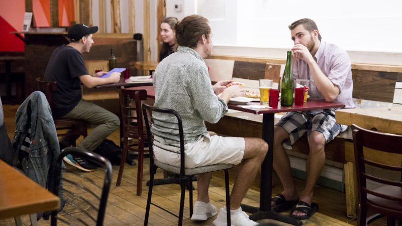 Nick Boucher (right) and Chris Calabrese enjoy slices of a Pizza Gutt plain pie at W/N W/N coffee bar on October 10, 2018. Boucher has enjoyed Chef Daniel Gutter's Detroit-style pizza on three occasions, while Calabrese is trying it for the first time. (Rachel Wisniewski for WHYY)