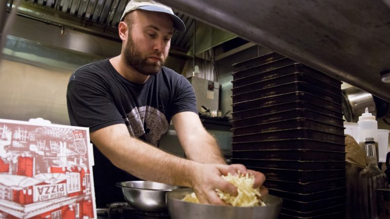 Chef Daniel Gutter grabs a handful of cheese as he prepares his signature Detroit-style pizzas in the kitchen of W/N W/N coffee bar. Gutter has been the resident chef at the bar since August 2017, with his business primarily located on nstagram.  (Rachel Wisniewski for WHYY)
