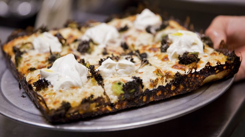 A server at W/N W/N coffee bar prepares to bring a broccoli and ricotta pie to a customer. Chef Daniel Gutter's signature 10-inch Detroit-style pizzas are highly sought after, with 25 pies reserved via instagram and 25 pies available via walk in from Wednesday to Sunday. (Rachel Wisniewski for WHYY)