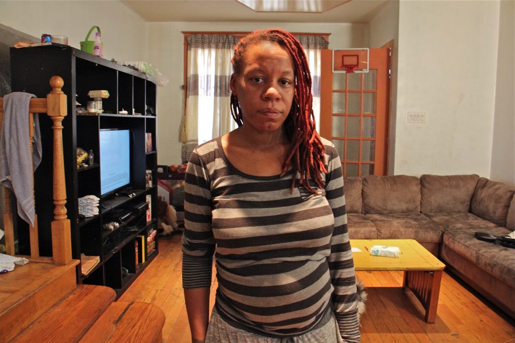 Sherri Lee stands in the living room of her rented home on Snyder Avenue. Plumbing issues there have forced her to seek another home for her family, which includes five children. (Emma Lee/WHYY)