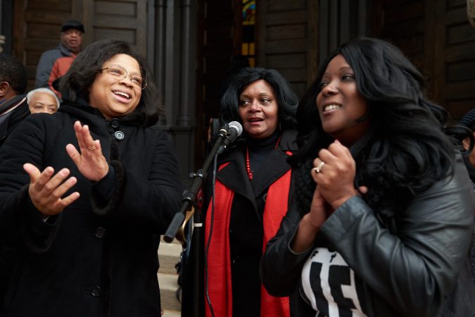 (From left) Joetta Cryer, Gloria Johnson, and Selah Wyche share a microphone and sing on the front steps of Mother Bethel A.M.E. Church on Sunday, Nov. 18, 2018. They are part of the mass choir who sang and cheered while thousands of participants in the 2018 Philadelphia Marathon ran past them on Sixth street. (Natalie Piserchio for WHYY)