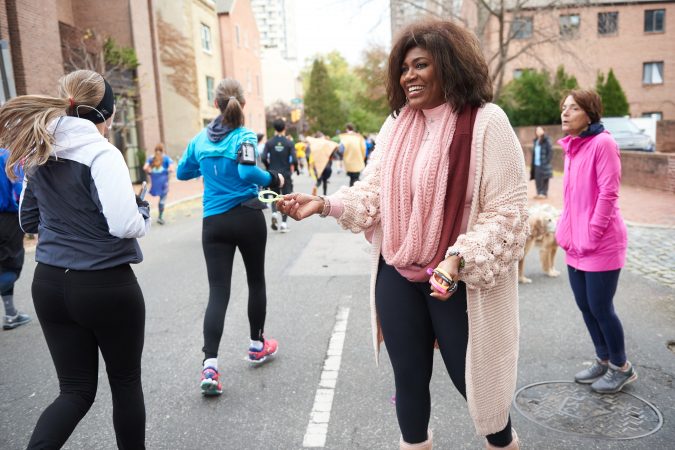 Leslie Tyler, Rev. Mark Kelly Tyler’s wife, hands out church wristbands to participants of the 2018 Philadelphia Marathon as they run past Mother Bethel A.M.E. Church and its singing choir. Being a runner herself, she found the marathon runners' energy particularly motivating. (Natalie Piserchio for WHYY)