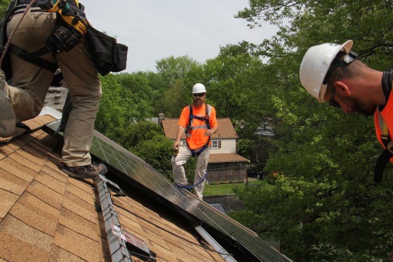 People install a solar panel on a roof.