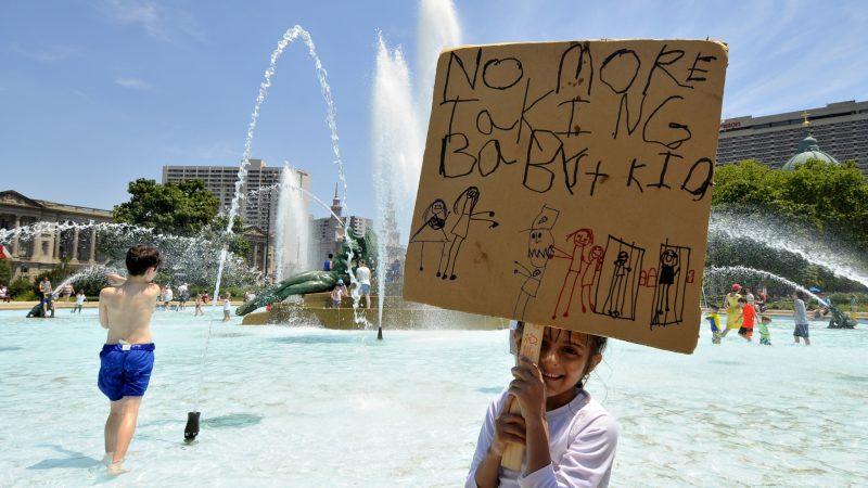 Olivia, 5, daughter of an undocumented immigrant father from Mexico, stands in the fountain holding a self-made sign. She's joined by her family as they take part in the End Family Deportation rally, on June 30, 2018. (Bastiaan Slabbers for WHYY)