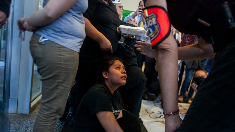 Under threat of arrest, Keyri Artillero Apolonio, 14, and her mother, Carmela Apolonio Hernandez, stand in front of an entrance at 2000 Market St., demanding a meeting with U.S. Sen.  Bob Casey on Oct. 10, 2018. Hernandez, an undocumented immigrant, took sanctuary in a North Philadelphia Church with her four children last December. (Brad Larrison for WHYY)