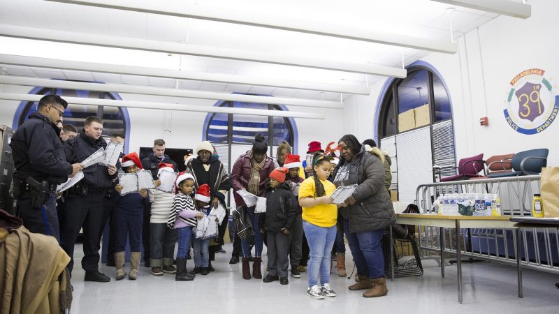 About ten Philadelphia police officers and twenty members of the Hunting Park community gather at the 39th Police District to sing Christmas carols on December 7. Crystal Cooper (right) and her granddaughter, Promise Cooper (second from right), attended the event so that the police officers could have the opportunity to 