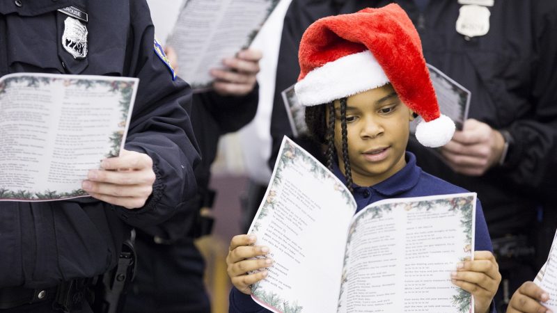 Jacqueline Tyler, 8, a ballet student at the Georgia E. Gregory Interdenominational School Of Music, sings Christmas carols alongside officers at the 39th Police District on December 7. Tyler and her grandmother, Marian (not pictured), have been coming to the annual event for three years 