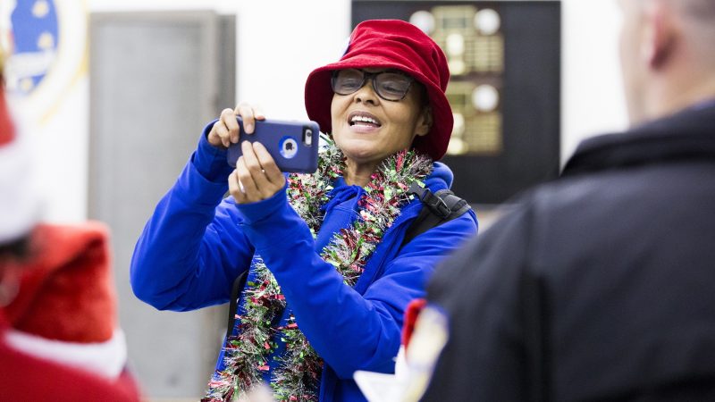 Susie Paige takes a photograph of community members and police officers who have joined together to sing Christmas carols at the 39th Police District on December 7. (Rachel Wisniewski for WHYY)